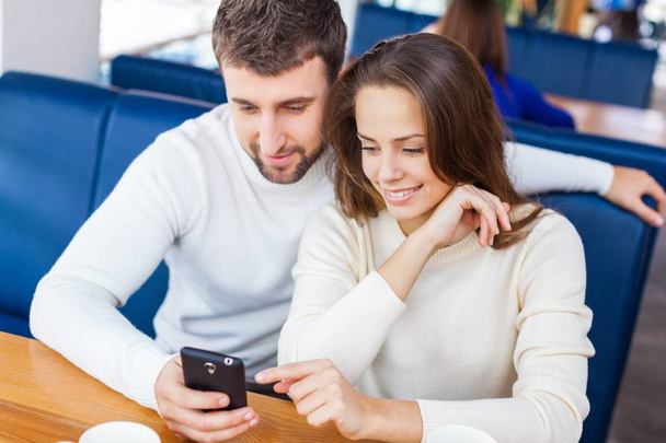 handsome man with young woman in fashion clothes using mobile on cafe background - Foto, Bild