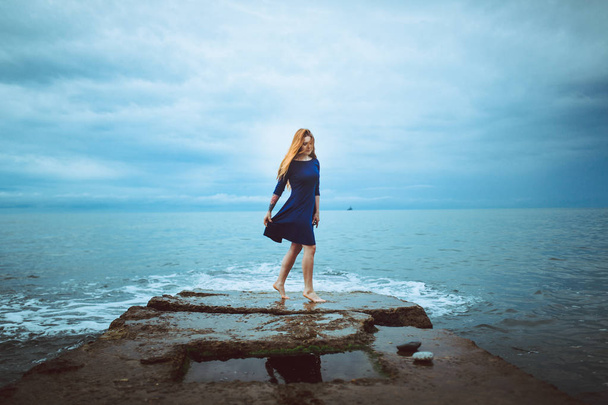 wyrażenie włos czerwony taniec w niebieskiej sukience na brzegu morza w pochmurny dzień odkryty - Zdjęcie, obraz