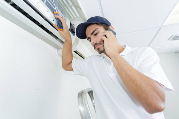 young handyman repairing air conditioning system calling for help - Foto, immagini