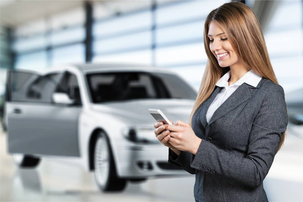 portrait of pretty young woman using phone near car - Photo, Image