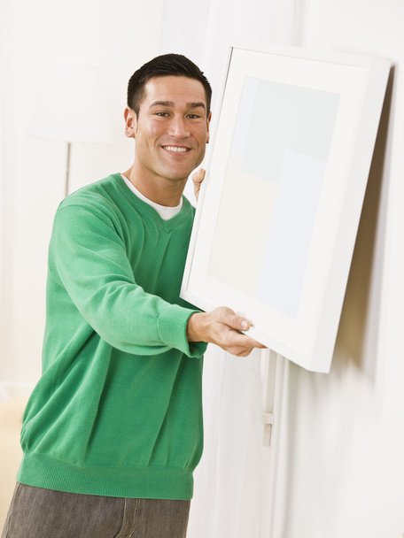 χαριτωμένο άνδρα που κρέμεται καμβά στον τοίχο διαμέρισμα - Φωτογραφία, εικόνα