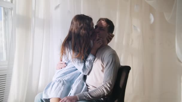 Молодий хлопець і дівчина сидять біля вікна в яскраво освітленій кімнаті, обіймаючи і цілуючи
 - Кадри, відео