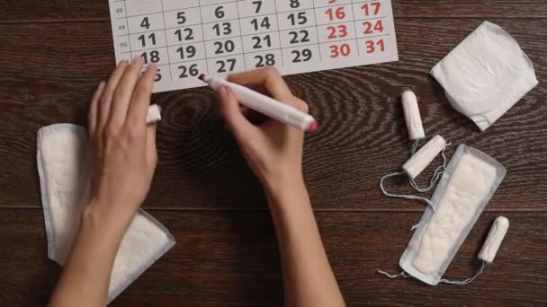 Dziewczyna oznacza dzień miesiączki na kalendarz i tampony higieniczne i uszczelki leżą w pobliżu - Materiał filmowy, wideo