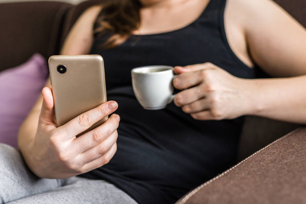 Person with mobile phone in hand and coffee on sofa at home, people's lifestyle and modern technology concept - Foto, Imagen