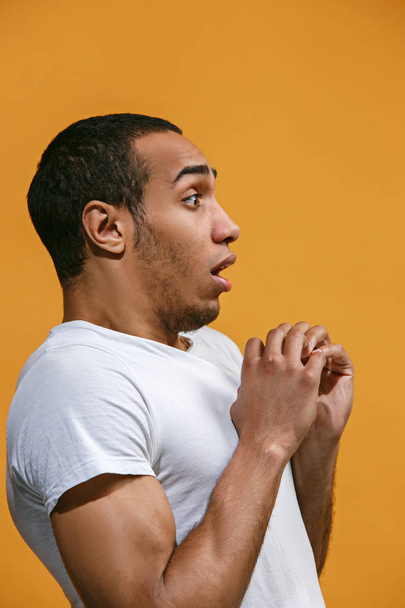 Doubtful Afro-American man is looking frightenedly against orange background - Фото, изображение