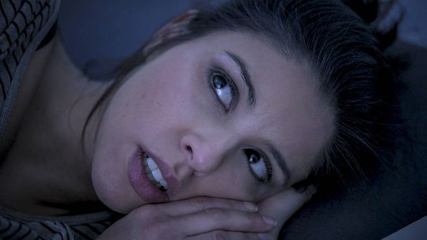 young beautiful sad and worried latin woman suffering insomnia and sleeping disorder problem unable to sleep late at night lying on bed awake  - Photo, Image