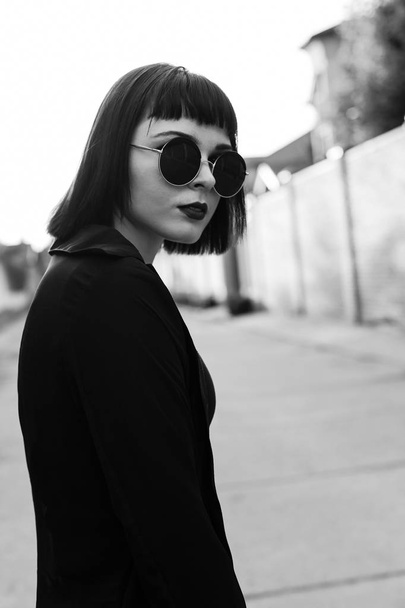 Monochrome portrait of young woman in round glasses walking on street - Photo, Image