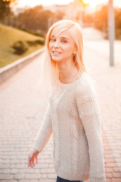 Smiling young blond woman walking on city street during sunset - Фото, зображення
