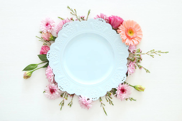 Top view of vintage white empty plate over spring flowers. Flat lay. - Foto, afbeelding