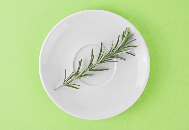 Twig of fresh rosemary in white plate on green background. Top v - Фото, зображення