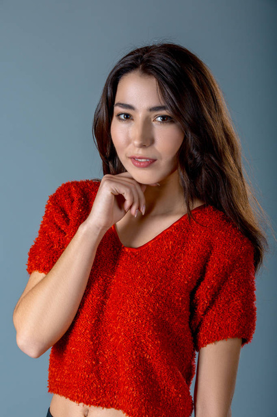 shot of pleased pretty woman with pleasant charming smile, dressed in red sweater, expresses positive emotions, over grey background. Facial expressions concept. - Fotoğraf, Görsel