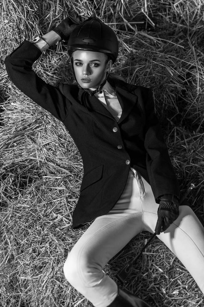 richly woman in equestrian suit and equipment lying on hay, sport and fashion concept  - Photo, Image