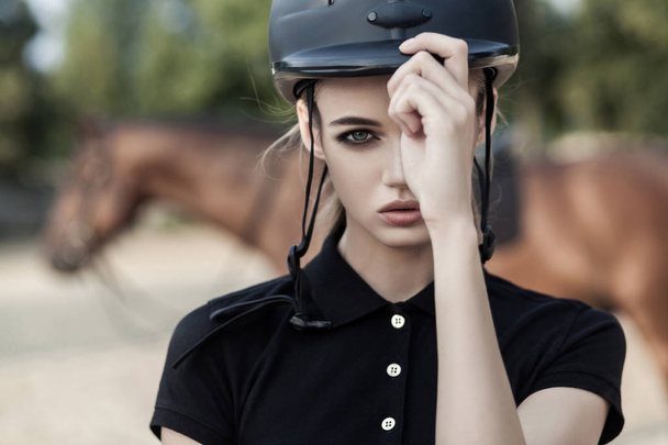 model dragen van Paardensport pak en apparatuur kijken camera met paard op achtergrond, sport en mode concept. - Foto, afbeelding