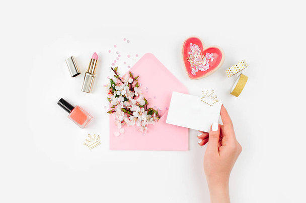 Woman hold card. Pink envelope with a spring flower arrangement and accessories. Flat lay, top view. - Foto, Imagen