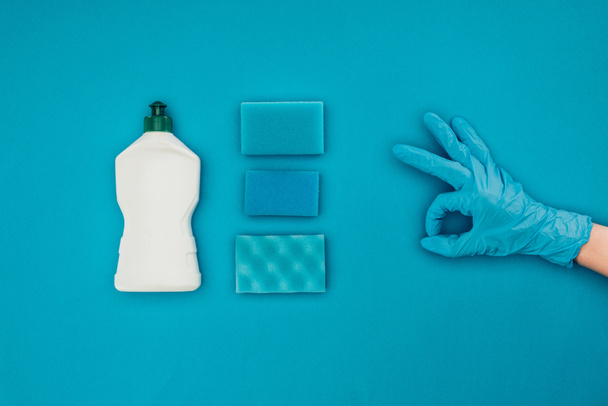 περικομμένη εικόνα της γυναίκας δείχνει εντάξει σημάδι στο ελαστικό προστατευτικό γάντι απομονώνονται σε μπλε - Φωτογραφία, εικόνα