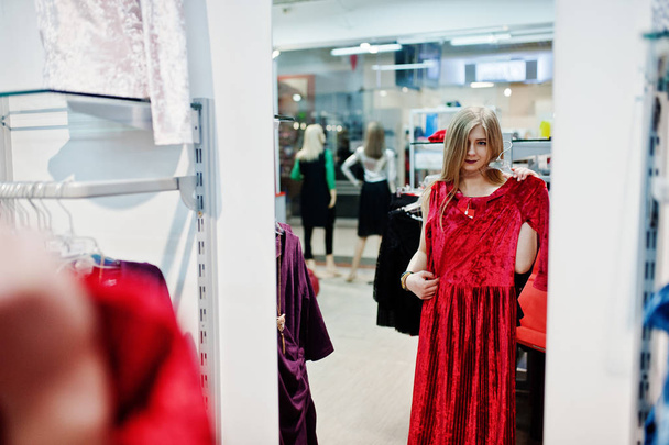 Blonde girl tries a red dress in the boutique, looking at the mi - Foto, immagini
