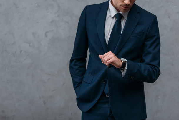 Oříznout záběr podnikatel v stylovém obleku při pohledu na hodinky před betonovou zeď - Fotografie, Obrázek