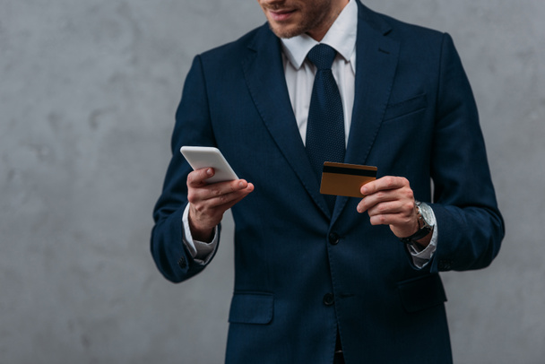 обрезанный снимок бизнесмена с помощью кредитной карты и смартфона, делающего электронные покупки
 - Фото, изображение