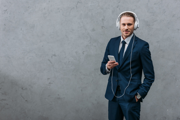 молодой бизнесмен слушает музыку с наушниками и смартфоном
 - Фото, изображение