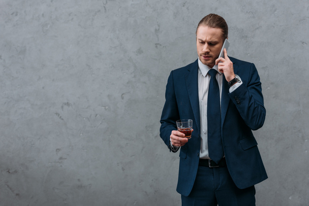 young serious businessman with glass of whiskey talking by phone - 写真・画像