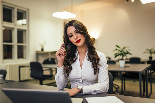 Image of beautiful businesswoman sitting at workdesk, holding pen. - Photo, Image