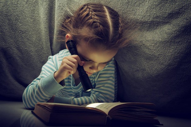 Petite fille lisant des contes de fées livre sous les couvertures à la veille
 - Photo, image