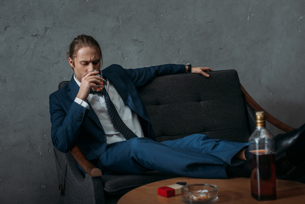 joven adicto al alcohol hombre de negocios beber whisky mientras está sentado en el sofá
 - Foto, Imagen