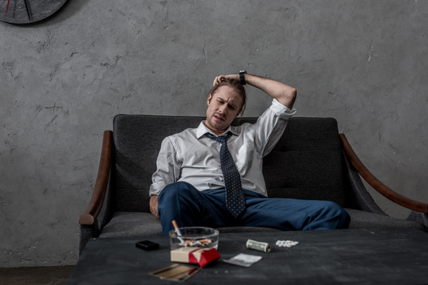 подавленный бизнесмен с наркотической зависимостью сидит на диване перед столом с наркотиками
 - Фото, изображение