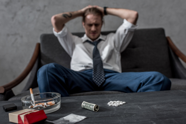 hombre de negocios deprimido con adicción a las drogas sentado en el sofá frente a la mesa con píldoras mdma
 - Foto, Imagen