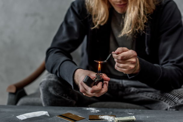 Schnappschuss eines süchtigen Junkies, der Heroin in einem Löffel mit Feuerzeug kocht - Foto, Bild