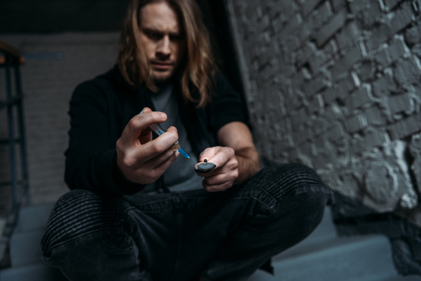 verslaafd junkie vullen spuit met heroïne van lepel - Foto, afbeelding
