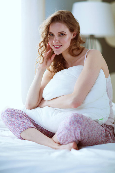 Young woman holding a pillow while sitting on her bed. - Foto, afbeelding