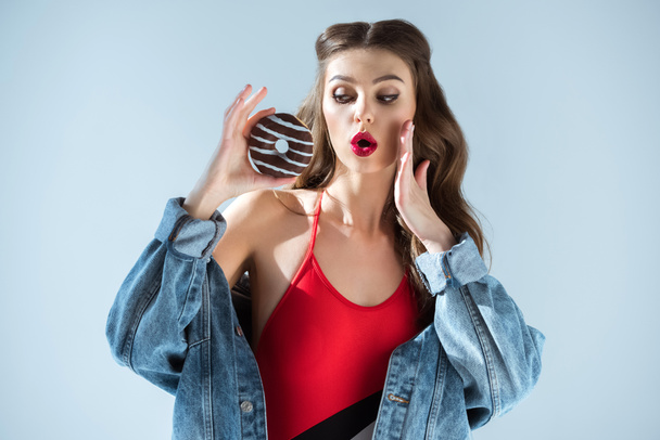 surprised sexy girl in red swimsuit looking at donut isolated on grey - Photo, Image