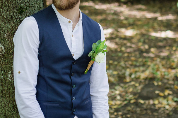Όμορφος κομψός γενειοφόρος γαμπρός με καρό κοστούμι στέκεται στη γέφυρα του δάσους. Κομψή φωτογραφία γαμήλιων γαμπρού. Ρουστίκ πορτραίτο χίπστερ. - Φωτογραφία, εικόνα