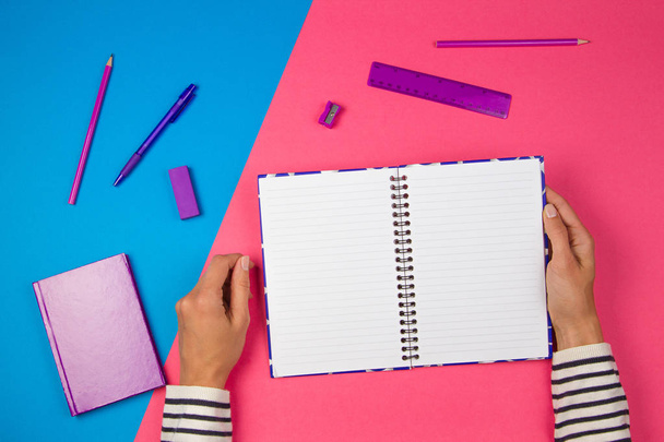 Vrouw handen met open notebook en kantoorbenodigdheden op kleurrijke achtergrond - Foto, afbeelding
