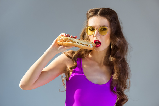 sexy attrayant fille en maillot de bain ultra violet manger hot dog et regarder la caméra isolé sur gris
 - Photo, image
