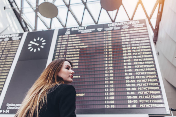 Jonge vrouw stond tegen vlucht scorebord in luchthaven - Foto, afbeelding