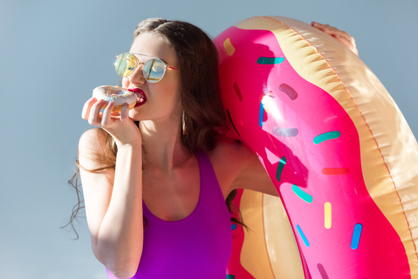 sexy attractive girl in ultra violet swimsuit eating doughnut isolated on grey - Photo, Image