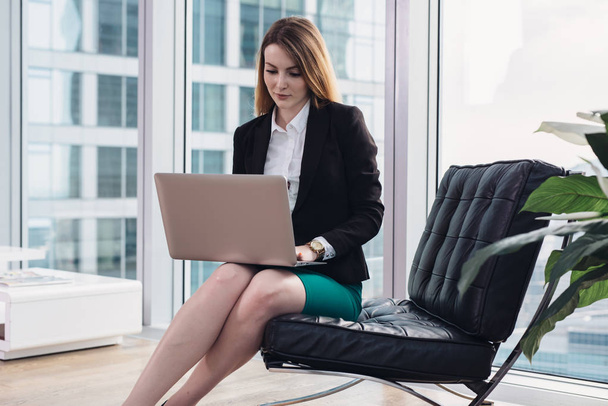 女性のチーフ ・ エコノミストは近代的なオフィスのアームチェアに座ってラップトップを使用してデータを分析します。 - 写真・画像