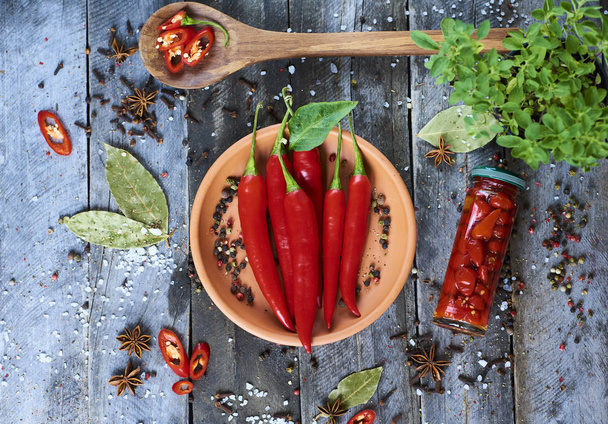 Čerstvé red hot chili papričky v misce s kořením a lžičkou na dřevěné rustikální pozadí, pohled shora - Fotografie, Obrázek
