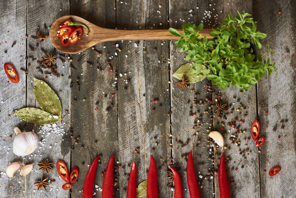 Fresh red hot chili peppers in bowl with spices and spoon on wooden rustic background, top view - Photo, Image