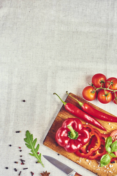 Ψιλοκομμένες κόκκινες πιπεριές σε ξύλο κοπής, με μπαχαρικά, βασιλικό, ρόκα, ντομάτες, μαχαίρι και κόκκινα πιπέρια τσίλι, το top view - Φωτογραφία, εικόνα