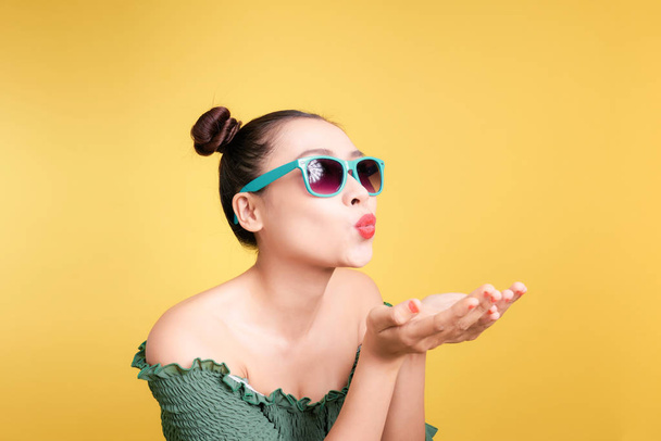 Mujer asiática de moda en gafas de sol de moda envía un beso contra el fondo amarillo brillante
 - Foto, imagen