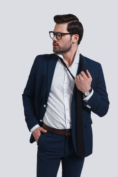 exhausted young man in full suit looking away and taking off his necktie in studio - Photo, Image