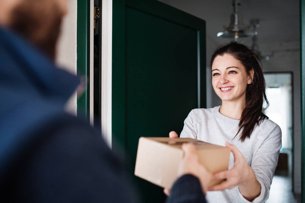 Woman receiving parcel from delivery man at the door. - 写真・画像