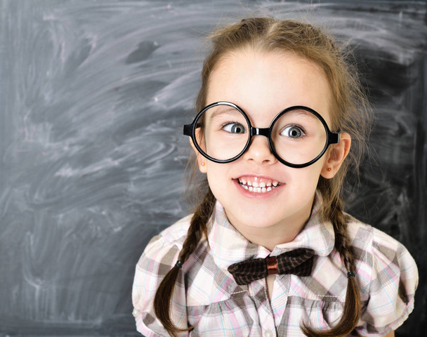 Cute funny liitle girl standing near blackboard in big glasses a - Фото, изображение