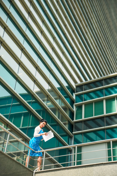Heureuse jeune femme d'affaires dans le centre-ville debout contre un immeuble de bureaux moderne
. - Photo, image