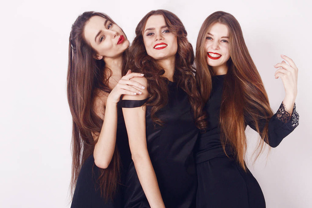 Beautiful young girls with make-up, red lips, pretty face . Womans on white background. Cheerful young womans wearing black dress, looking at camera with joyful and charming smile. Long hair - Photo, Image