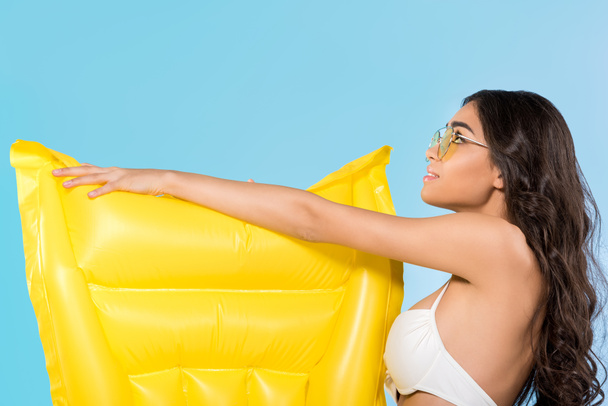 beautiful young woman in yellow sunglasses posing with yellow inflatable mattress, isolated on blue  - Фото, зображення