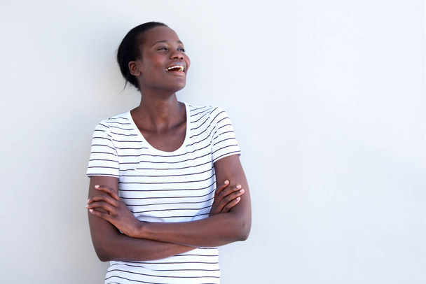 Porträt einer glücklichen afrikanisch-amerikanischen Frau, die mit von weißer Wand verschränkten Armen lacht - Foto, Bild